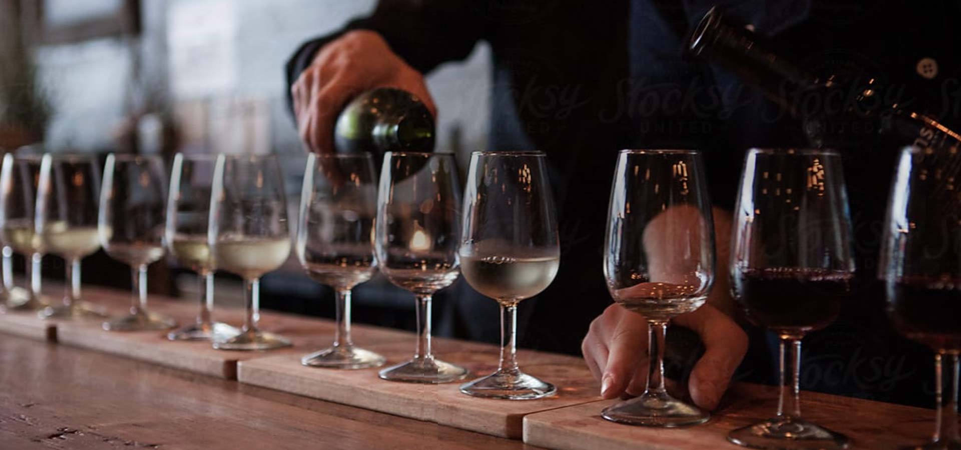 Close up of server pouring glasses of wine in a row.
